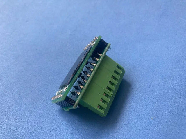 Two stacked green PCBs — display board on top showing the small OLED screen, connector board below with a large green screw terminal block visible from the side